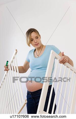 Stock Photograph - Pregnant woman putting together baby bed. Fotosearch