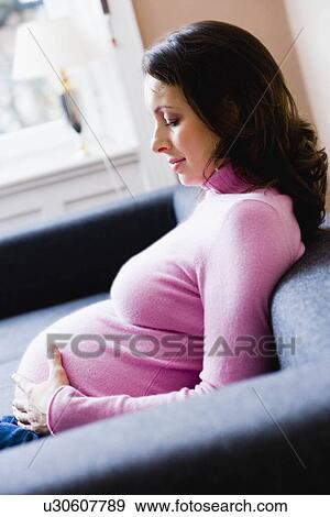 Stock Photo - Pregnant woman sitting on couch. Fotosearch