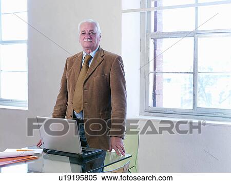 Stock Photography - Senior executive standing at table. Fotosearch