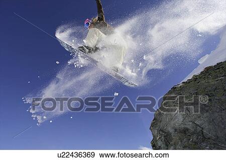 Snowboarder jumping off a rock View Large Photo Image Stock Photo - Snowboarder jumping off a rock. Fotosearch