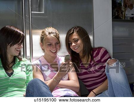 Stock Image - Teen girls laugh at phone photo. Fotosearch
