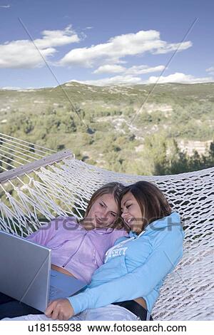 Stock Photo - Teen girls look laptop in hammock. Fotosearch