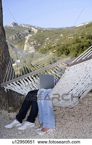 Stock Image - Teen legs in hammock with laptop. Fotosearch