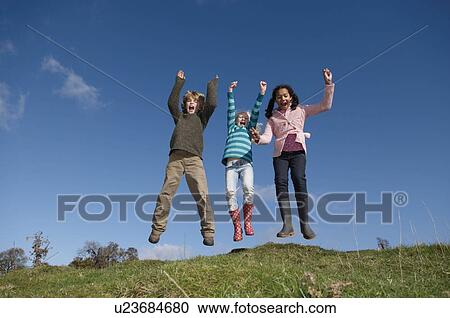 Stock Image - Three children jumping on hill. Fotosearch