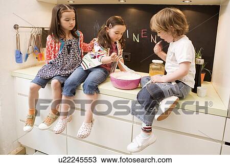 Stock Image - Two girls and boy cooking. Fotosearch
