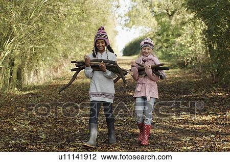 Stock Image - Two girls carrying firewood in country. Fotosearch