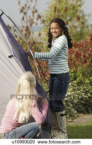 Stock Image - Two girls erecting tent. Fotosearch