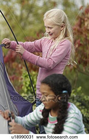 Stock Image - Two girls erecting tent. Fotosearch