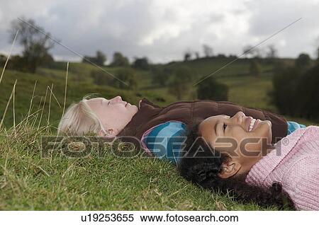 Two girls lying on grass looking at sky View Large Photo Image Stock Photography - Two girls lying on grass looking at sky. Fotosearch