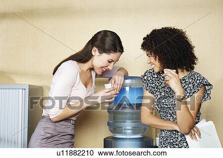 Stock Image - Two women laughing by water cooler. Fotosearch