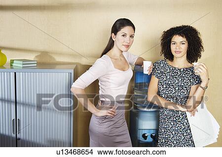 Picture - Two women standing by water cooler. Fotosearch