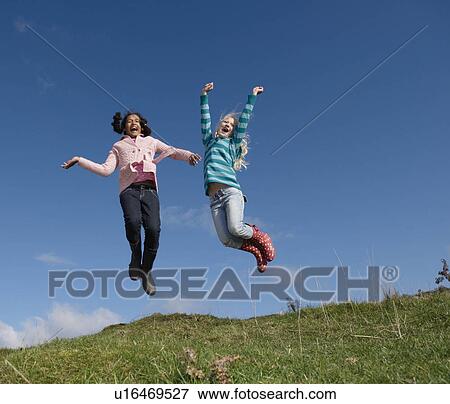 Two young girls jumping on hill View Large Photo Image Stock Photo - Two young girls jumping on hill. Fotosearch