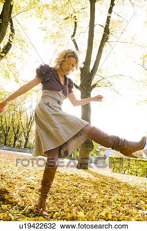 Stock Image - Woman dancing within heaps of leaves. Fotosearch