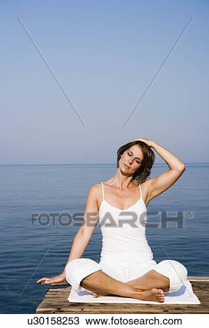 Stock Image - Woman doing yoga on a pier. Fotosearch