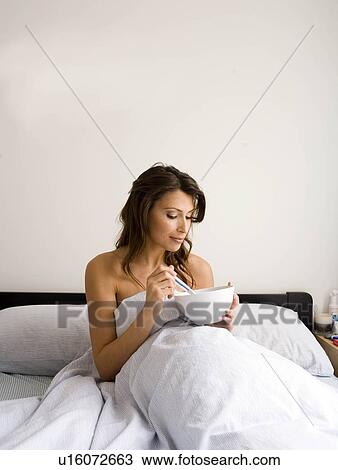 Stock Image - Woman eating cereal in bed. Fotosearch