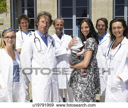 Stock Photo - "Woman holding her baby, doctors around". Fotosearch