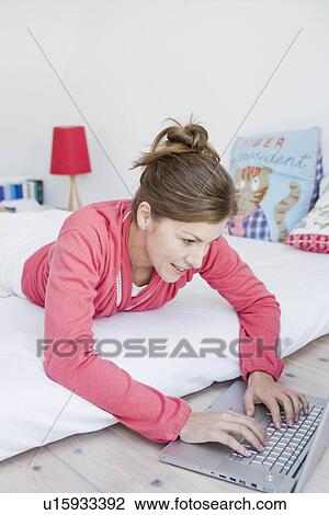 Woman lying on bed with laptop View Large Photo Image Stock Image - Woman lying on bed with laptop. Fotosearch