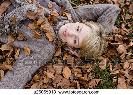Stock Image - Woman lying within heaps of dry leaves. Fotosearch