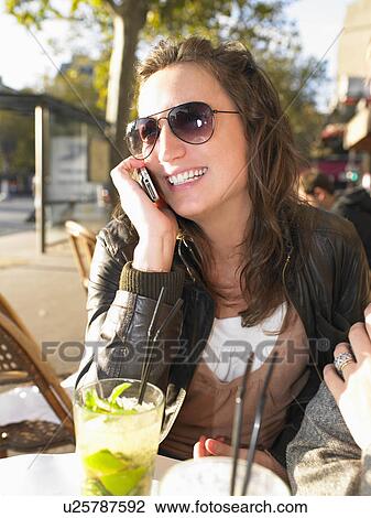 Stock Image - Woman on phone on terrace of café. Fotosearch