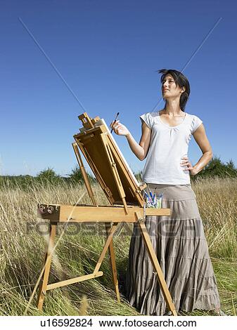 Picture - "Woman painting in a field, smiling". Fotosearch