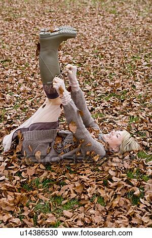 Stock Image - Woman playing within heaps of dry leaves. Fotosearch