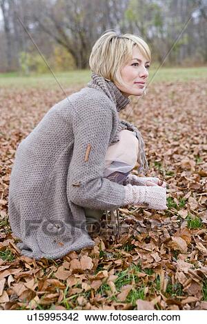Stock Image - Woman playing within heaps of dry leaves. Fotosearch