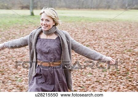 Stock Image - Woman playing within heaps of dry leaves. Fotosearch