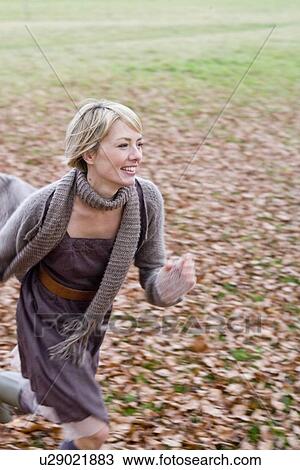 Stock Image - Woman playing within heaps of dry leaves. Fotosearch