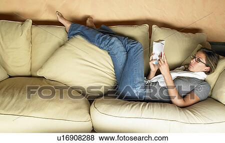 Stock Photo - Woman reading a book on sofa. Fotosearch