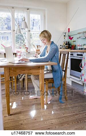 Woman sitting in kitchen at laptop View Large Photo Image Stock Photo - Woman sitting in kitchen at laptop. Fotosearch