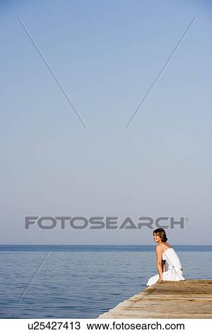 Stock Image - Woman sitting on a pier. Fotosearch