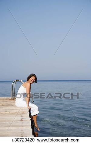 Stock Image - Woman sitting on a pier. Fotosearch