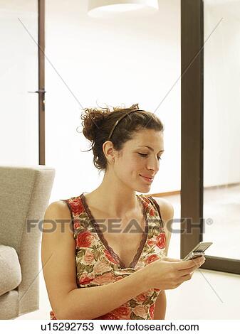 Stock Image - "Woman sitting on floor, texting". Fotosearch