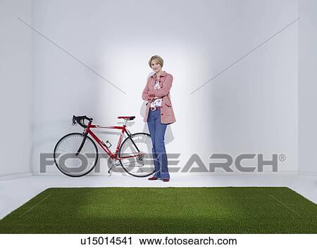 Stock Image - Woman standing next to bicycle. Fotosearch