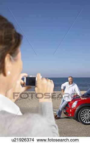 Woman taking photo of man by car View Large Photo Image Picture - Woman taking photo of man by car. Fotosearch