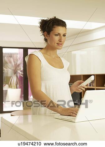 Stock Image - Woman using laptop on kitchen work top. Fotosearch