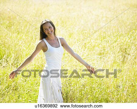 Stock Image - "Woman walking in a field, smiling". Fotosearch