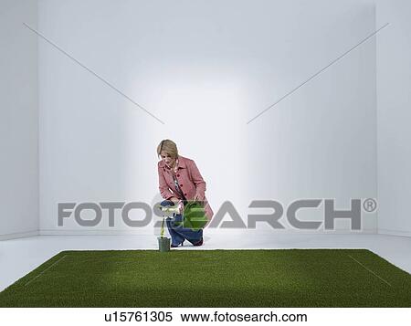 Stock Photography - Woman watering plant in a green office. Fotosearch