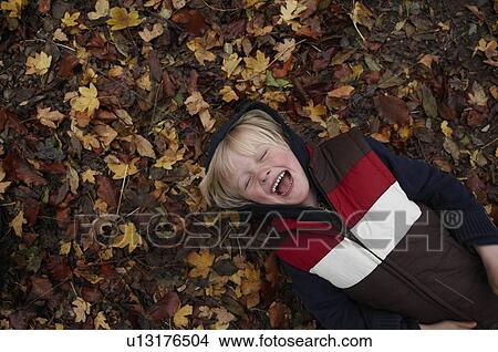 Picture - Young boy lying on autumn leaves. Fotosearch