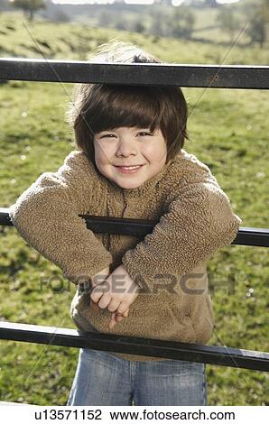 Stock Image - Young boy on gate in countryside. Fotosearch