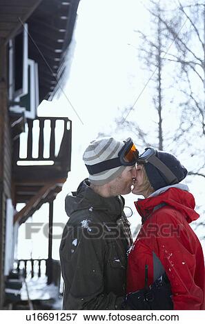 Stock Photo - Young couple in front of chalet kissing. Fotosearch