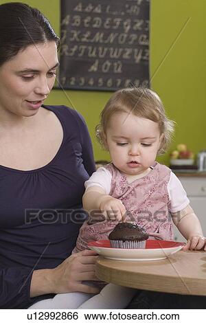 Young girl on mothers lap with muffin View Large Photo Image Stock Photograph - Young girl on mothers lap with muffin. Fotosearch