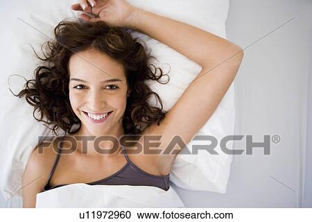 Stock Image - Young woman in bed smiling to camera. Fotosearch