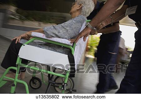 Stock Image - Attendant helping patient on wheelchair. Fotosearch