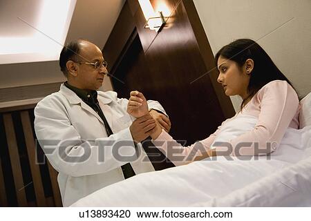 Stock Image - Doctor checking the pulse of a patient. Fotosearch