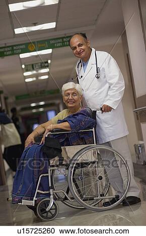 Stock Image - Doctor helping patient on wheelchair. Fotosearch