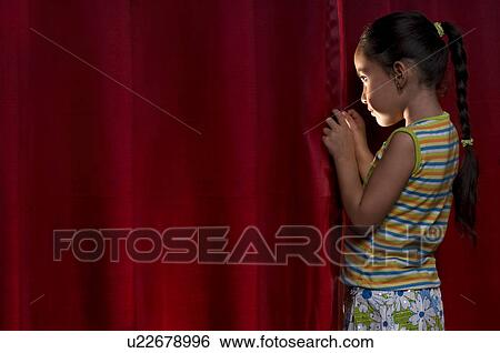 Stock Photograph - Little girl peeking out from behind the curtain. Fotosearch