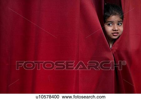 Stock Image - Little girl peeking out from the curtain. Fotosearch