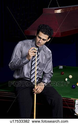 Stock Image - Man applying chalk to cue stick. Fotosearch
