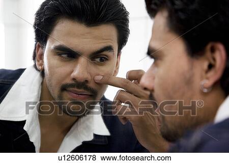 Stock Photo - Man checking his eye in the mirror. Fotosearch